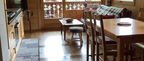 Interior acogedor de una cabaña con una mesa de comedor de madera, sillas, una pequeña cocina y un ventanal con vistas al exterior.
