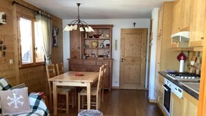 A cozy cabin interior with a dining table, chairs, a kitchen area with a stove, and a living room with a sofa and a coffee table.