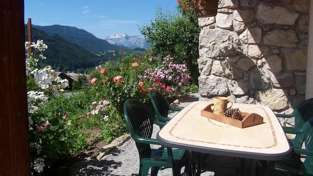 An outdoor patio with a stone wall, a table with chairs, and a view of mountains. - Ground floor, terrace, parking, tv, ski locker, 39m², Le Grand Bornand (Le Grand-Bornand)