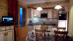 A kitchen with wooden cabinets, a dining table with chairs, a television, and a refrigerator. - Ground floor, terrace, parking, tv, ski locker, 39m², Le Grand Bornand (Le Grand-Bornand)