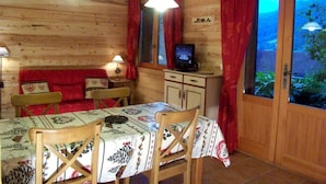 A wooden cabin with a dining table, chairs, a television, and a view through a glass door. - Ground floor, terrace, parking, tv, ski locker, 39m², Le Grand Bornand (Le Grand-Bornand)