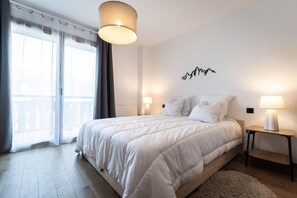 A bedroom with a large bed, two bedside tables, a hanging light fixture, and a wall decal. - 50m from ski slopes, balcony, tv, 115m², Montalbert (La Plagne)