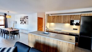 A modern kitchen with wooden cabinets, a black refrigerator, and a dining area with a table and chairs. - 50m from ski slopes, balcony, tv, 115m², Montalbert (La Plagne)