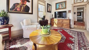 A living room with a round wooden coffee table, a white sofa, a large painting, a wooden cabinet, and a patterned rug. - Spacious Downtown Spot-Sleeps 8! (Arcata)