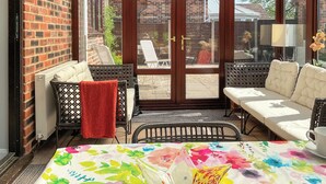 Eine sonnendurchflutete Terrasse mit Korbmöbeln, einem weißen Sofa und einer blumigen Tischdecke.