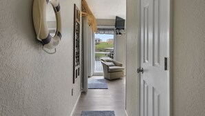 A hallway with a lifebuoy on the wall, a chair by a window, and a door leading to a balcony. - Waterfront 2BR/2BA Condo, Walk-Out Deck to Lake, Pools & Hot Tub (Village of Four Seasons)