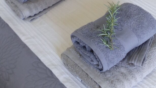 A neatly made bed with two folded towels, each with a sprig of rosemary. - Cozy studio with air conditioning; secure parking; countryside near the city (Avignon)