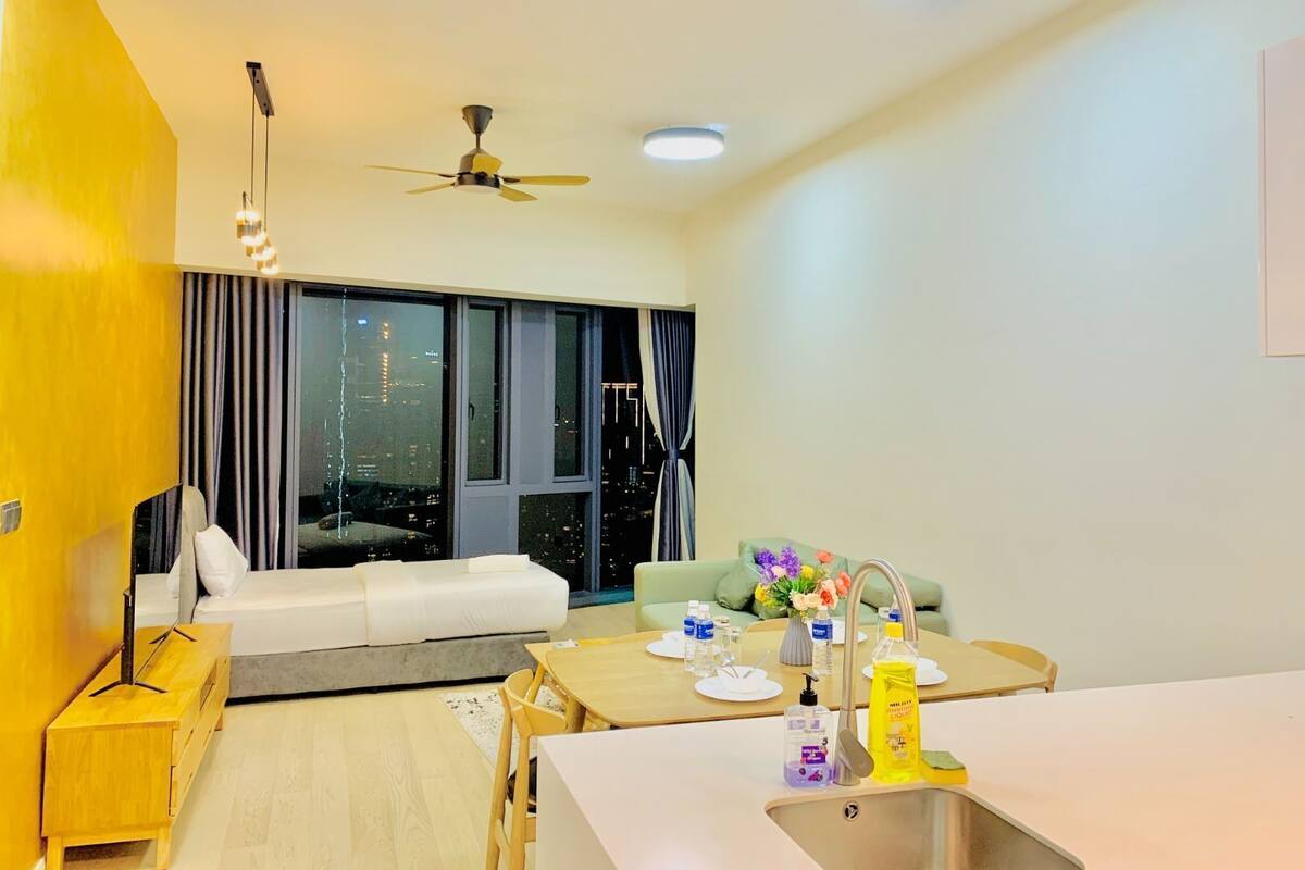 A modern hotel room with a bed, a desk, a dining table, and a large window with curtains.