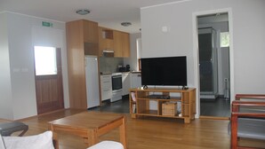 Una sala de estar moderna con una mesa de centro de madera, un televisor de pantalla plana sobre un mueble bajo, y una cocina con armarios y electrodomésticos de madera.