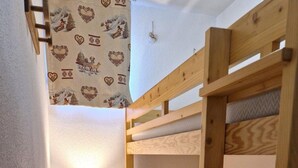 Une petite pièce étroite, avec un lit superposé, une petite table avec une lampe et un radiateur.