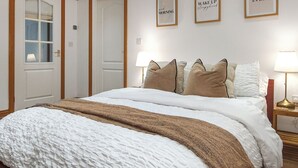 Una cama bien tendida con una manta blanca y marrón, un cabecero de madera y una pared con tres citas motivacionales enmarcadas.