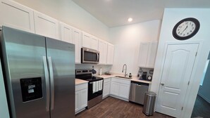 A modern kitchen with white cabinets, stainless steel appliances, a microwave, and a clock on the wall. - Charming 3-bedroom house with WiFi, AC in terrific Palm Coast (Palm Coast)