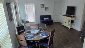 A dining area with a wooden table, chairs, and a blue bowl. There is a sofa and a TV in the background. - Charming 3-bedroom house with WiFi, AC in terrific Palm Coast (Palm Coast)