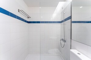 A modern bathroom with white tiles, a glass shower enclosure, and a white bathtub.