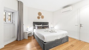 A modern bedroom with a grey upholstered bed, a bedside table with a lamp, a wall-mounted air conditioner, and a door with a handle. - GuestReady - Charming Retreat near the Cathedral (Vila Nova de Gaia)