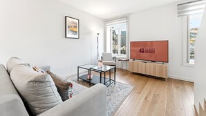 A modern living room with a sofa, a coffee table, a TV, and a window with a view. - GuestReady - Charming Retreat near the Cathedral (Vila Nova de Gaia)