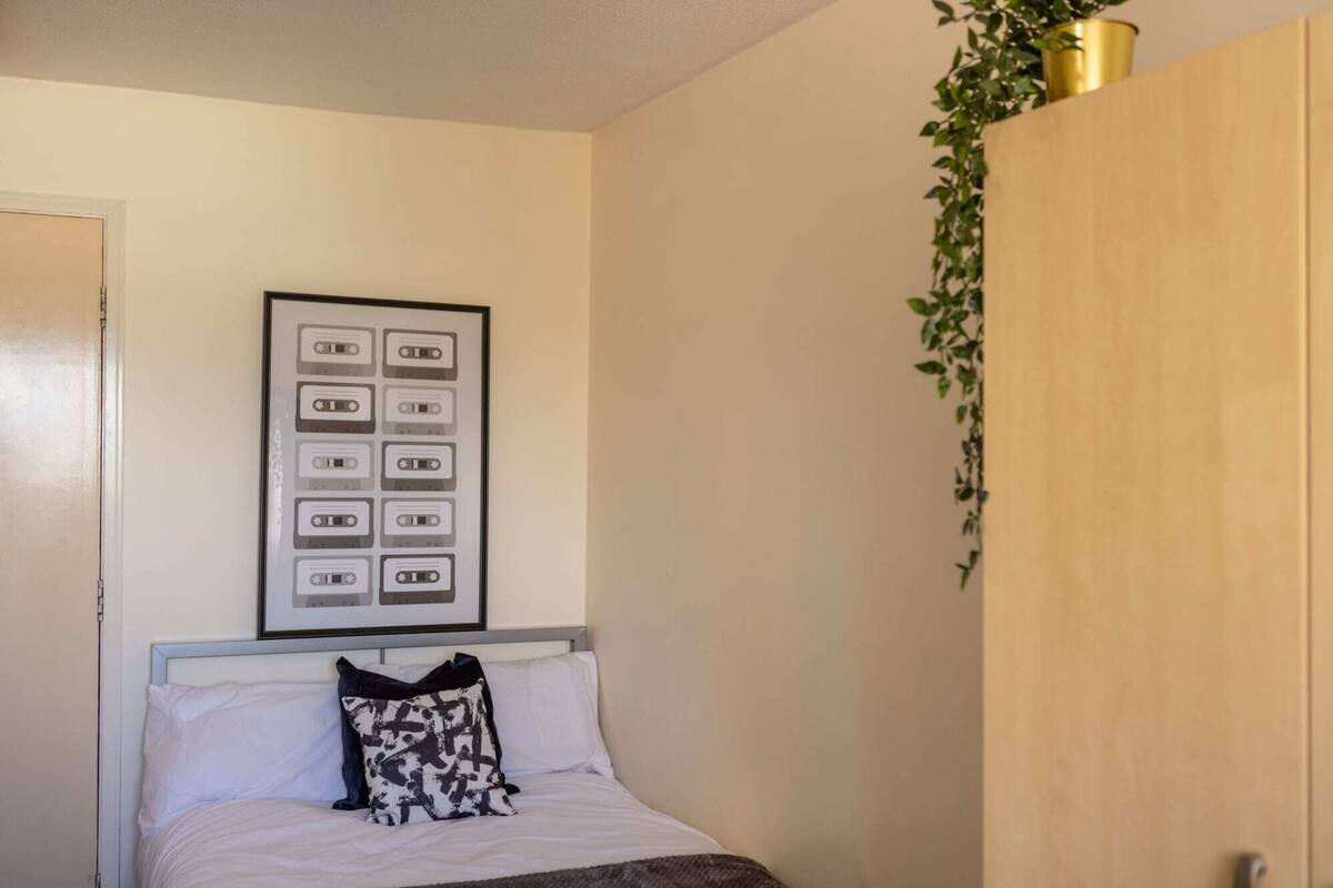 Una camera da letto con un letto, un quadro con cassette, una pianta e un armadio in legno.