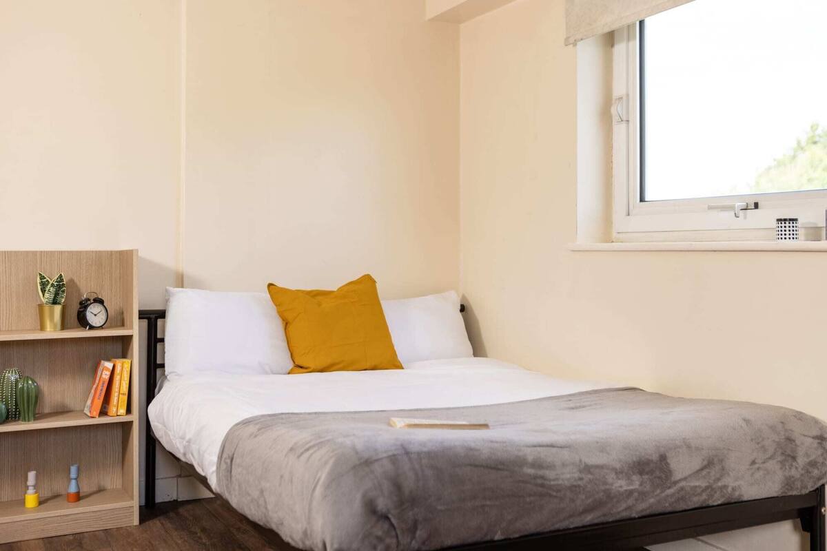 Una camera da letto con un letto, una finestra, uno scaffale con libri e una pianta e un comodino.