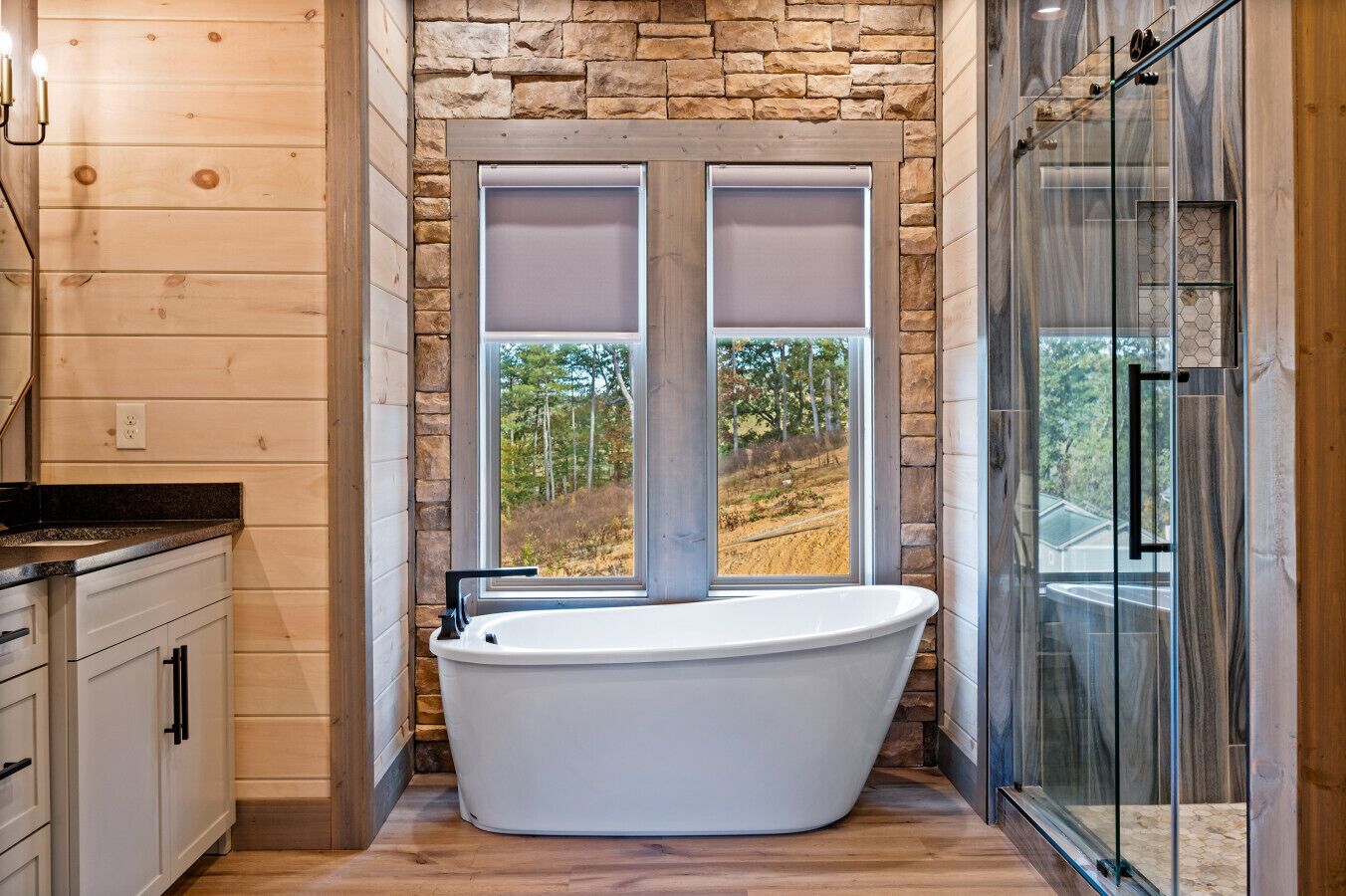 Ein modernes Badezimmer mit freistehender Badewanne, einer Duschkabine aus Glas und einem großen Fenster mit Blick ins Freie.