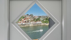 A view through a window of a coastal town with buildings along the water, a bridge, and a boat. - GuestReady - Riverside Retreat with Terrace Views (Vila Nova de Gaia)