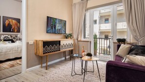 A modern living room with a sofa, a small coffee table, a TV mounted on the wall, and a balcony with a view of the building's exterior. - Charming 1-bedroom apartment with WiFi, AC in gorgeous Jerusalem (Jerusalem)