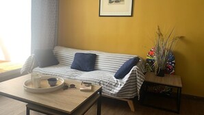 Ein gemütliches Wohnzimmer mit einer gestreiften Couch, einem kleinen Tisch mit einer Schüssel und Büchern, einem gerahmten abstrakten Kunstwerk an der Wand und einer Zimmerpflanze auf einem Beistelltisch.