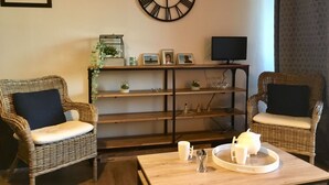 Ein Wohnzimmer mit zwei Korbstühlen, einem Couchtisch mit Tablett, einer großen Wanduhr und einem Regal mit Dekoration.