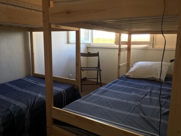 A dormitory room with two bunk beds, a chair, and a window.