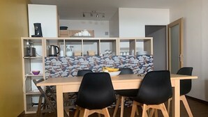 Ein Essbereich mit Holztisch und schwarzen Stühlen, im Hintergrund eine Küche und eine fliesenförmige Wandverkleidung.