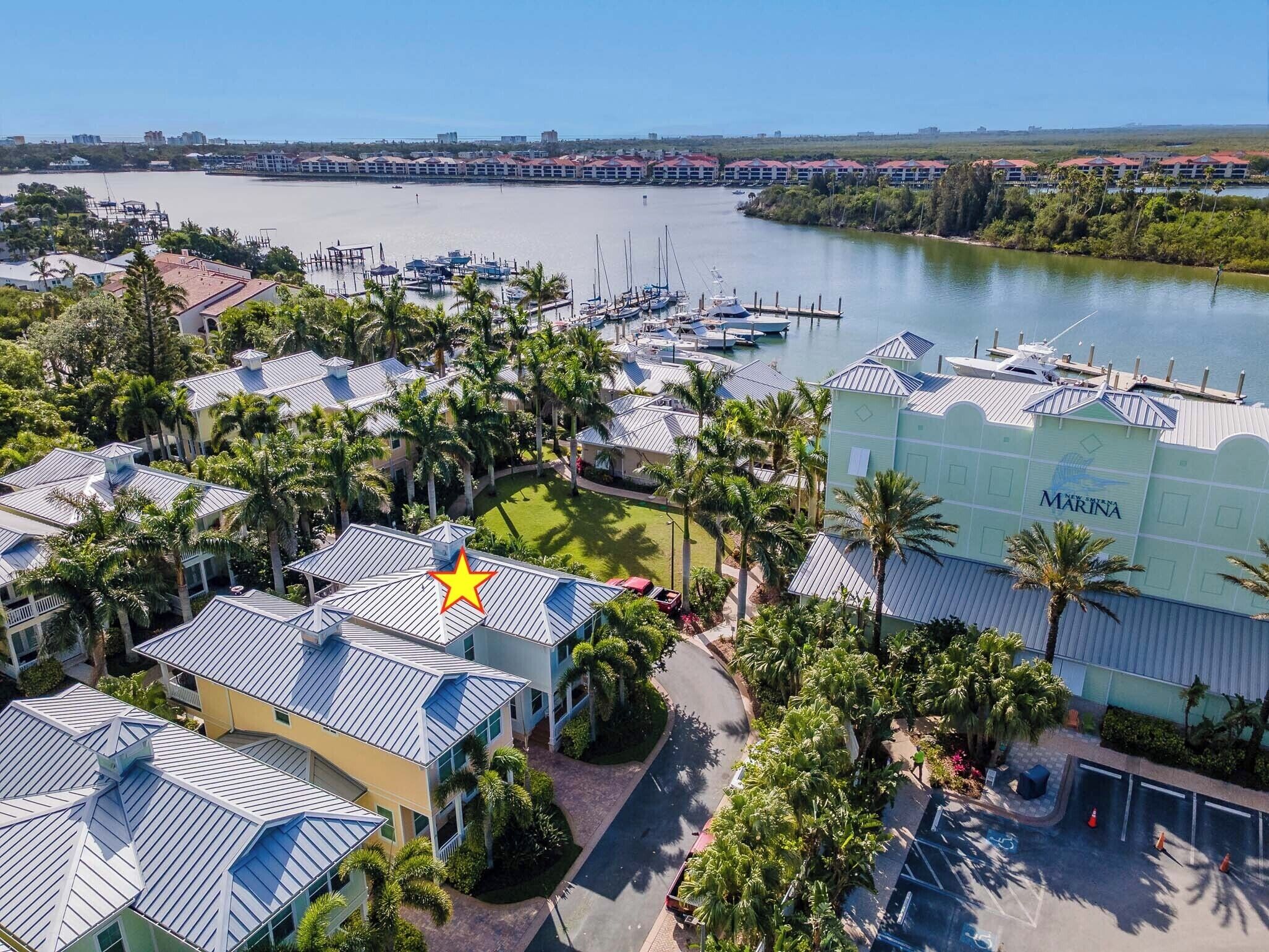 A marina with boats docked, surrounded by buildings with blue roofs and palm trees.