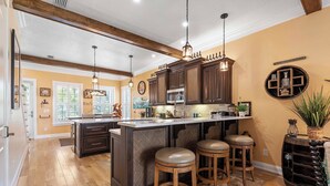 Una cocina con armarios de madera oscura, una isla central con taburetes, iluminación colgante y un estante circular en la pared.