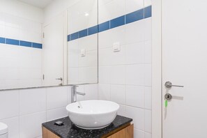 A bathroom with white tiles, a white sink, a mirror, and a door with a key in the lock. - GuestReady - Beautiful Riverside Retreat (Vila Nova de Gaia)