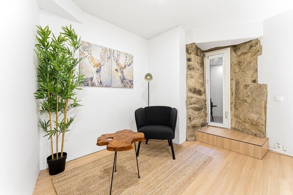 A modern living room with a black armchair, a wooden coffee table, a large potted plant, and a wall with abstract art.