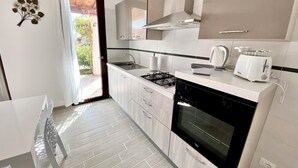 A modern kitchen with white cabinetry, a gas stove, a built-in oven, and a toaster. - Villasimius, Vacation House, with private garden, Casagora (Sardegna)