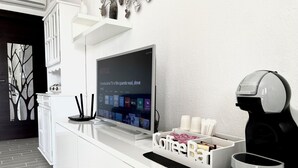 A modern reception area with a flat-screen TV displaying a Netflix interface, a coffee machine, and a white counter with a coffee station. - Villasimius, Vacation House, with private garden, Casagora (Sardegna)