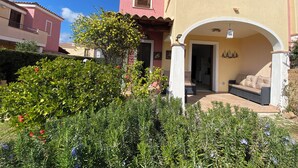 A two-story house with a balcony, a covered porch, and a garden with various plants and flowers. - Villasimius, Vacation House, with private garden, Casagora (Sardegna)