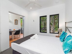 A hotel room with a bed, a desk, and two windows with blinds. - Holiday-Apartment Ocean Sound (Port Douglas)