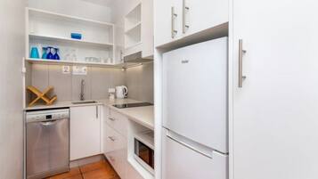Una cucina compatta con mobili bianchi, forno a incasso, lavastoviglie e frigorifero.