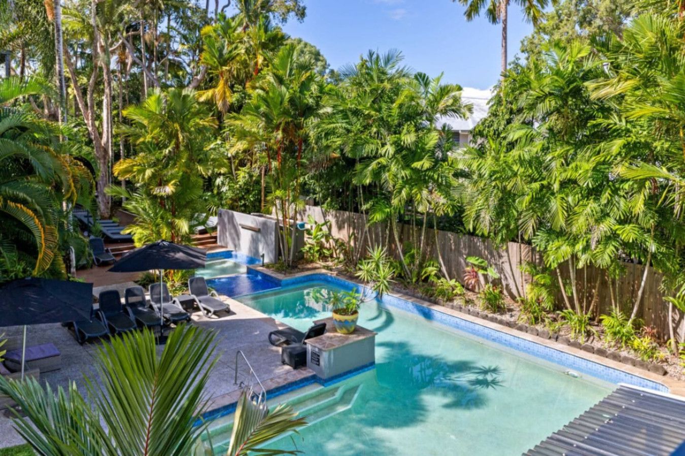 Un área de piscina con sillones de descanso y sombrillas, rodeada de exuberante vegetación tropical.