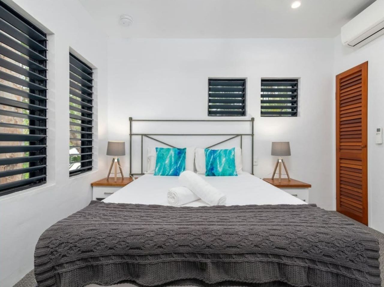 Un dormitorio moderno con una cama grande, dos mesitas de noche con lámparas, un cabecero y una ventana con persianas.