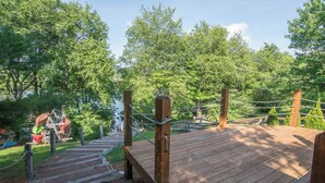 Een houten terras met een touwbalustrade, omringd door weelderige groene bomen.