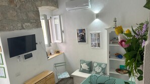 Une pièce comprenant une télévision, un petit bureau, une chaise, une armoire en bois, une table verte et une étagère avec des fleurs.