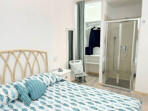 Ein Schlafzimmer mit einem Bett, einem Nachttisch, einem Spiegel, einem Kleiderschrank und einer Duschkabine.