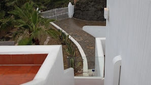 A rooftop terrace with a curved stone pathway, white walls, and a metal railing.