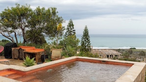A rectangular pool with a tiled edge, surrounded by stone tiles and potted plants.