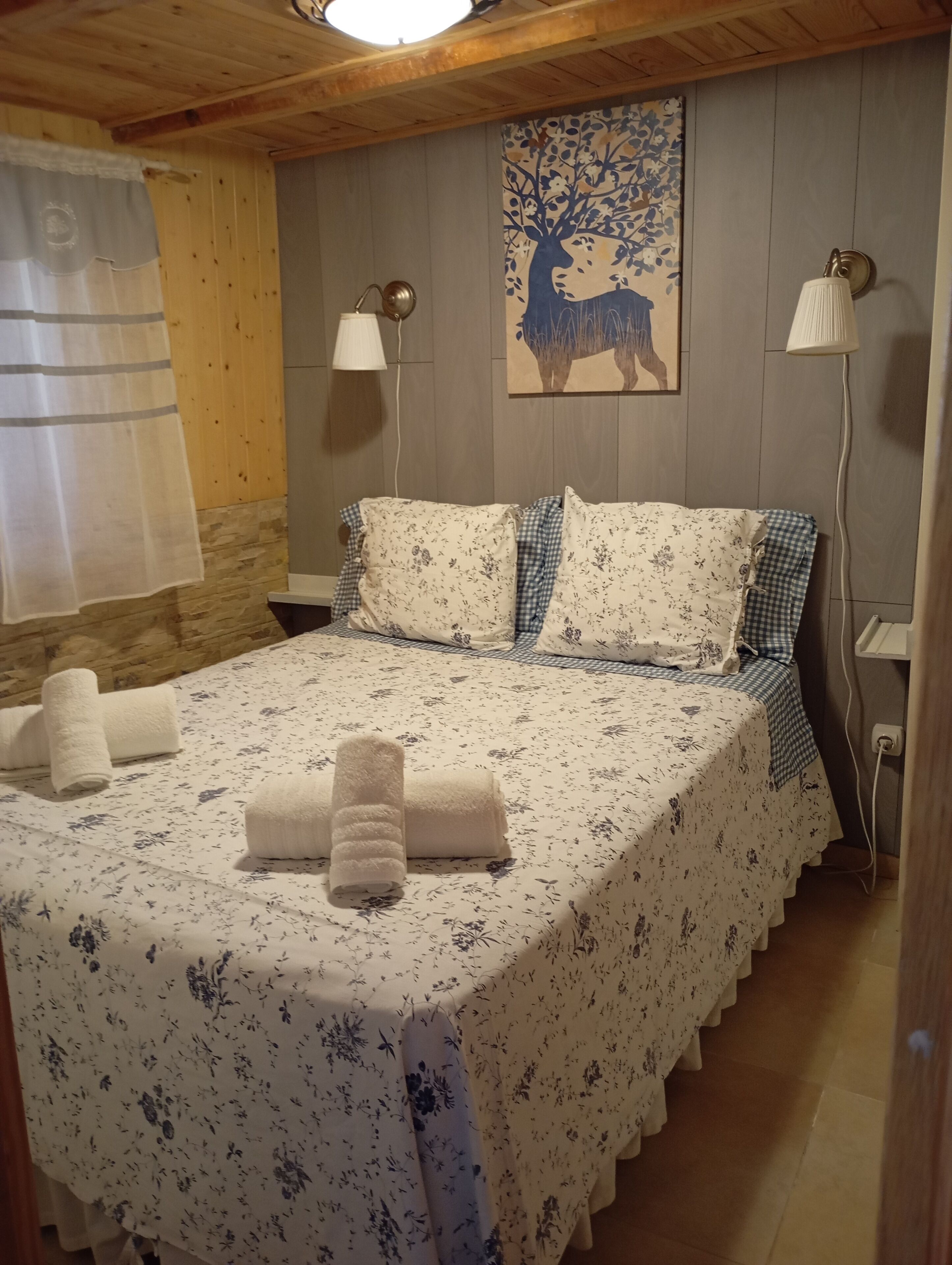 Una habitación con una cama, dos lámparas, un cuadro y una ventana con cortina.