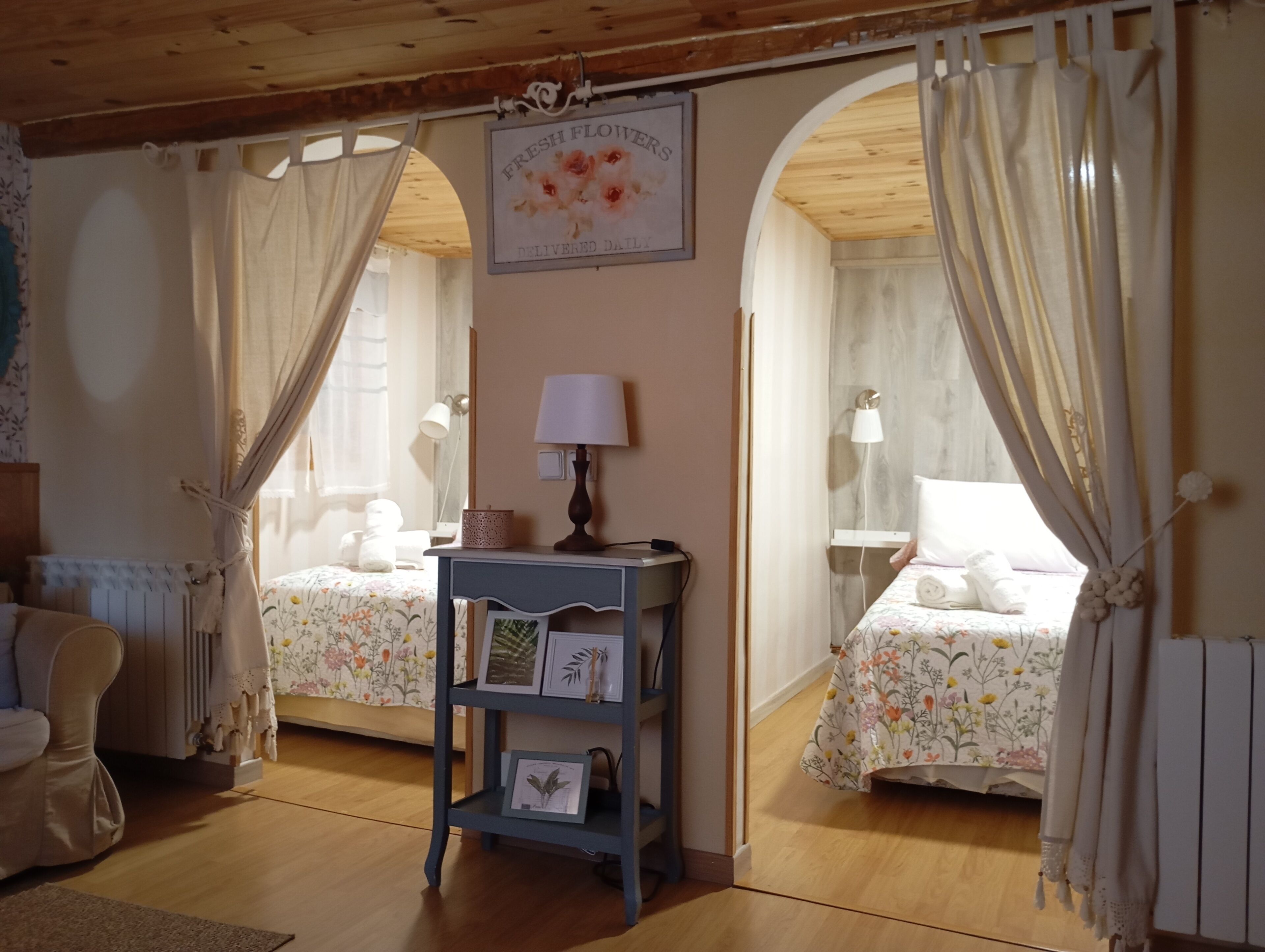 Een kamer met twee bedden, een kleine tafel met een lamp, een ingelijst schilderij en een bord boven de bedden.