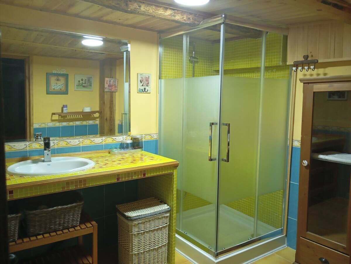 A bathroom with a glass-enclosed shower, a sink with a tiled backsplash, and wicker baskets.