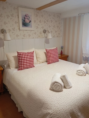 A neatly made bed with checkered pillows, a white knitted blanket, and rolled towels.