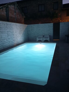 A rectangular swimming pool with a light blue water surface, surrounded by a brick wall and a stone building in the background. - La Mansion de la Toba (La Toba)